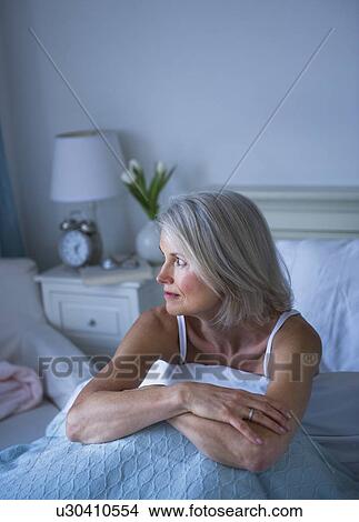 Picture - Senior woman sitting in bed and suffering from insomnia. Fotosearch