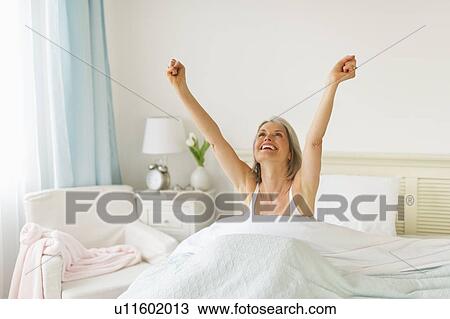 Stock Image - Senior woman stretching in bedroom in morning. Fotosearch
