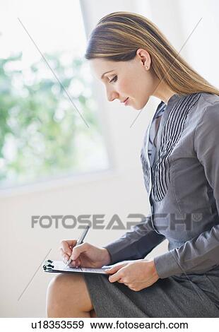 Side view of young business woman sitting and making notes View Large Photo Image Stock Photo - Side view of young business woman sitting and making notes. Fotosearch