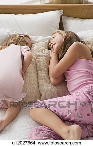 Picture - Sisters (8-9, 12-13) lying together on bed. Fotosearch