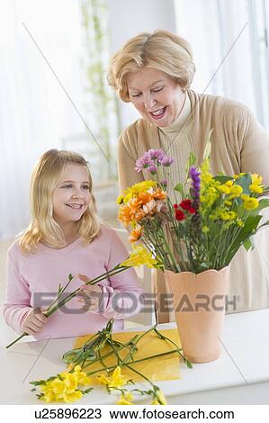 Stock Image - Smiling senior woman arranging flowers with granddaughter (8-9). Fotosearch