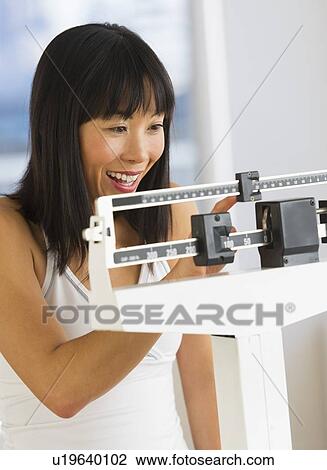 Stock Image - Smiling woman checking her weight. Fotosearch