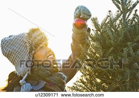 Stock Image - Smiling woman decorating Christmas tree. Fotosearch