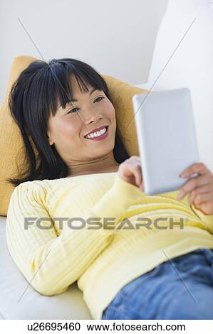 Smiling woman lying on sofa and using digital tablet View Large Photo Image Stock Image - Smiling woman lying on sofa and using digital tablet. Fotosearch