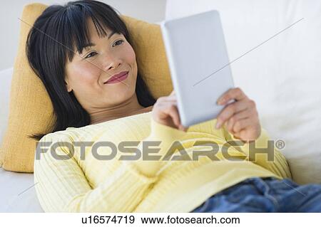 Smiling woman lying on sofa and using digital tablet View Large Photo Image Stock Photo - Smiling woman lying on sofa and using digital tablet. Fotosearch
