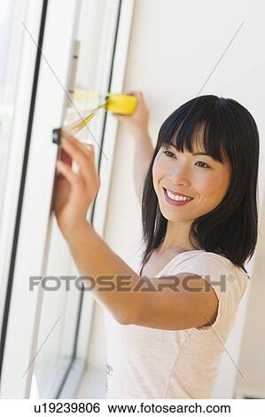 Stock Photograph - Smiling woman measuring window . Fotosearch