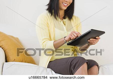 Smiling woman on sofa using digital tablet View Large Photo Image Picture - Smiling woman on sofa using digital tablet. Fotosearch