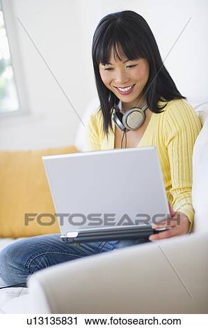 Smiling woman sitting on sofa and using laptop View Large Photo Image Stock Image - Smiling woman sitting on sofa and using laptop. Fotosearch