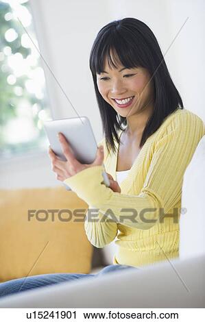 Stock Image - Smiling woman sitting on sofa and using digital tablet. Fotosearch