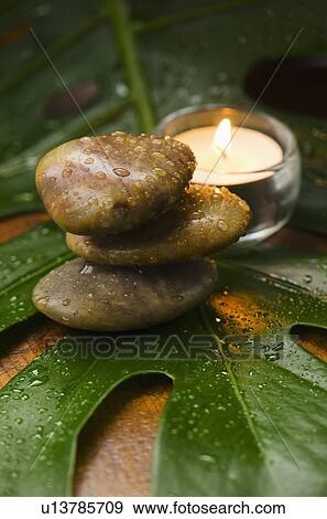 Stock Photo - Spa stones and candle on tropical leaf, studio shot. Fotosearch