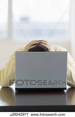 Stressed man sitting at desk behind laptop with head in hands View Large Photo Image Stock Photo - Stressed man sitting at desk behind laptop with head in hands. Fotosearch