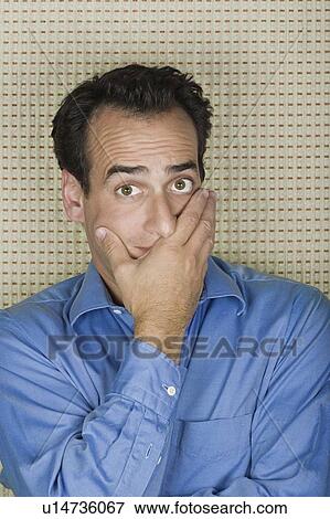 Stock Photo - Studio portrait of mid adult man covering mouth with hand. Fotosearch
