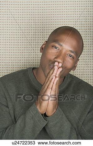 Stock Image - Studio portrait of mid adult man with hands clasped over mouth. Fotosearch