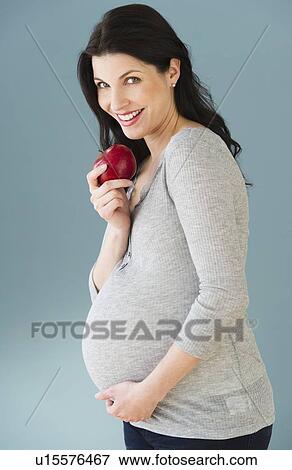 Stock Photo - Studio portrait of pregnant woman eating apple. Fotosearch