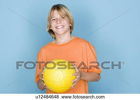 Stock Photo - Studio portrait of teenage (16-17) boy holding ball. Fotosearch
