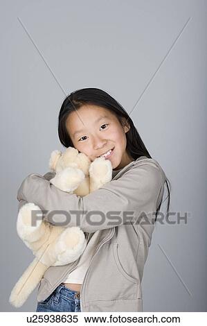 Stock Photography - Studio portrait of teenage Chinese girl (16-17) hugging teddy bear. Fotosearch