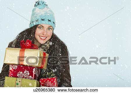 Stock Image - Studio portrait of woman in winter clothing carrying presents. Fotosearch