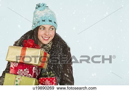 Stock Photo - Studio portrait of woman in winter clothing carrying presents. Fotosearch