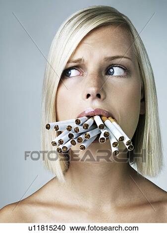 Stock Image - Studio portrait of young woman with mouthful of cigarettes. Fotosearch