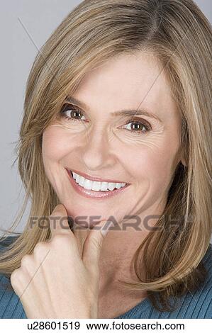 Stock Photo - Studio shot portrait of mature woman with hand on chin, close-up. Fotosearch