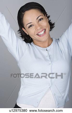 Stock Image - Studio shot portrait of mid adult woman with arms raised, waist up. Fotosearch