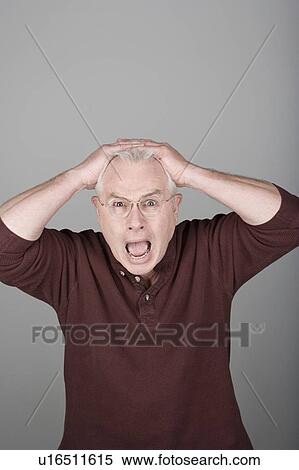 Stock Photography - Studio shot portrait of senior man with head in hands and open mouth, waist up. Fotosearch