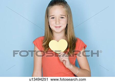 Stock Image - Studio shot portrait of teenage girl holding hart, head and shoulders. Fotosearch