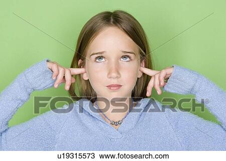 Stock Image - Studio shot portrait of teenage girl with fingers in ears, head and shoulders. Fotosearch
