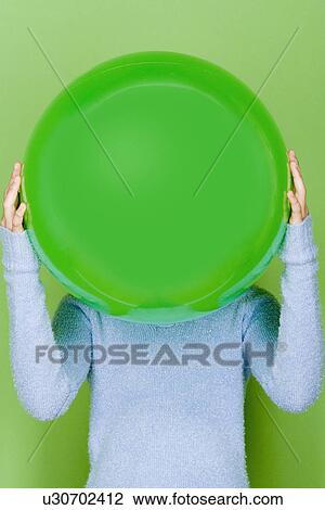 Stock Image - Studio shot portrait of teenage girl holding ball in front of her face, waist up. Fotosearch