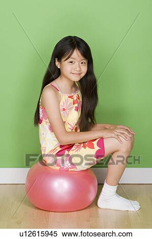 Stock Photography - Studio shot portrait of teenage girl sitting on ball, full length. Fotosearch