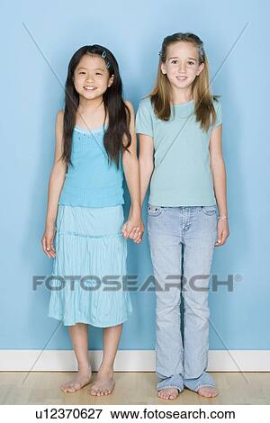 Stock Photo - Studio shot portrait of two teenage girls holding hands, full length. Fotosearch