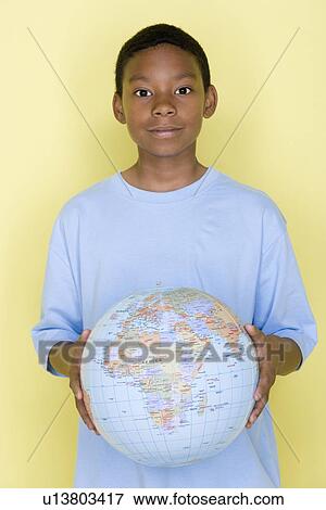 Stock Photo - Studio shot portrait of young man holding globe ball, waist up. Fotosearch
