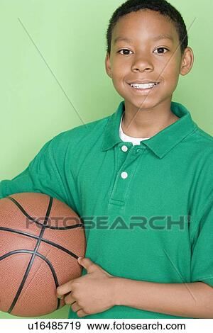 Stock Photo - Studio shot portrait of young man holding basket ball, waist up. Fotosearch