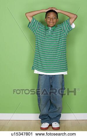 Stock Image - Studio shot portrait of young man with hands behind head, full length. Fotosearch