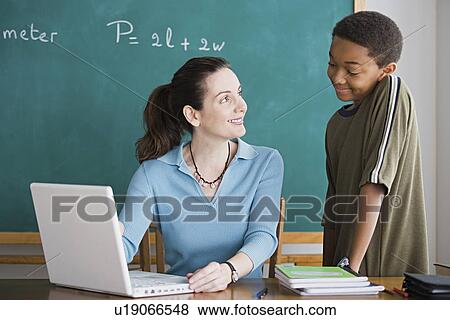 Teacher talking to schoolboy while using laptop View Large Photo Image Stock Photo - Teacher talking to schoolboy while using laptop. Fotosearch
