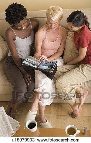 Stock Image - Three girlfriends looking at photo album. Fotosearch