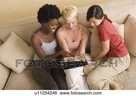 Stock Photograph - Three girlfriends looking at photo album. Fotosearch
