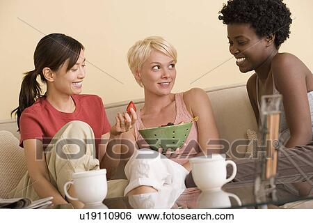 Stock Photograph - Three girlfriends relaxing on sofa. Fotosearch