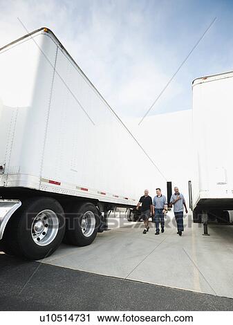 Stock Image - Three men walking between trucks. Fotosearch