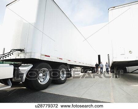 Stock Image - Three men walking between trucks. Fotosearch