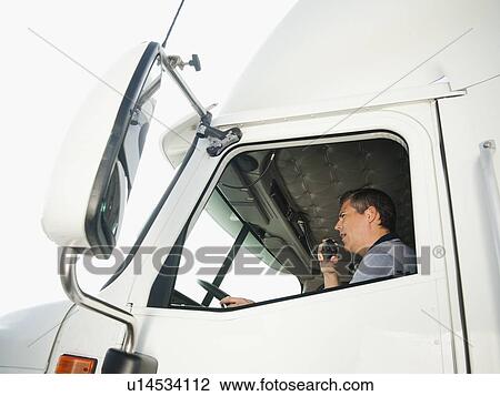 Stock Image - Truck driver sitting in truck and talking on CB radio. Fotosearch