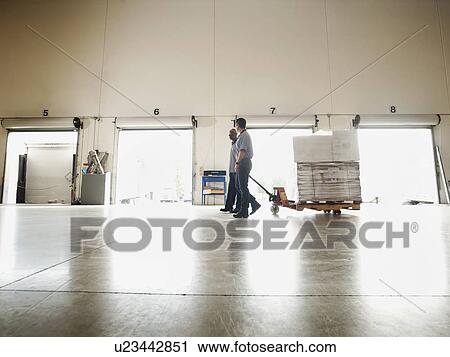 Two men pulling hand truck across warehouse View Large Photo Image Stock Image - Two men pulling hand truck across warehouse. Fotosearch
