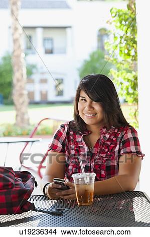 Picture - USA, California, La Quinta, Young woman using phone in outdoor cafe. Fotosearch