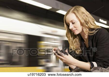 Stock Image - USA, California, Los Angeles, Woman sending text messages on subway station. Fotosearch