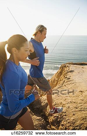 Stock Image - USA, California, San Diego, Man and woman jogging along sea coast. Fotosearch