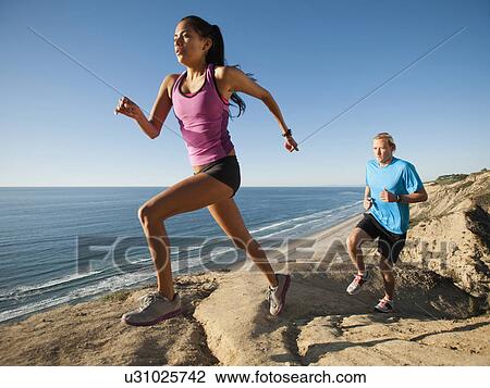 Stock Image - USA, California, San Diego, Man and woman jogging along sea coast. Fotosearch