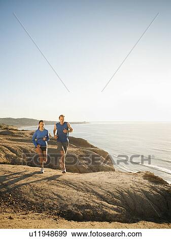 Stock Photo - USA, California, San Diego, Man and woman jogging along sea coast. Fotosearch