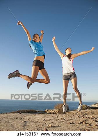 Stock Photo - USA, California, San Diego, Two women jumping at sea coast. Fotosearch