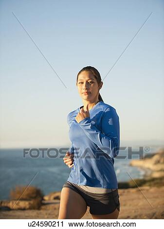 Stock Image - USA, California, San Diego, Woman jogging along sea coast. Fotosearch