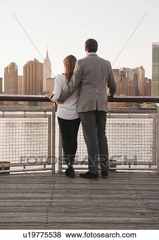 USA, New York, Long Island City, Rear view of young couple standing on boardwalk, Manhattan skyline in background View Large Photo Image Stock Photo - USA, New York, Long Island City, Rear view of young couple standing on boardwalk, Manhattan skyline in background. Fotosearch